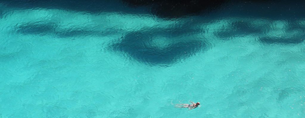 A man swimming in the pristine blue ocean waters near the beach in Mallorca, Spain, after a successful video production shoot, enjoying the relaxing and refreshing environment.