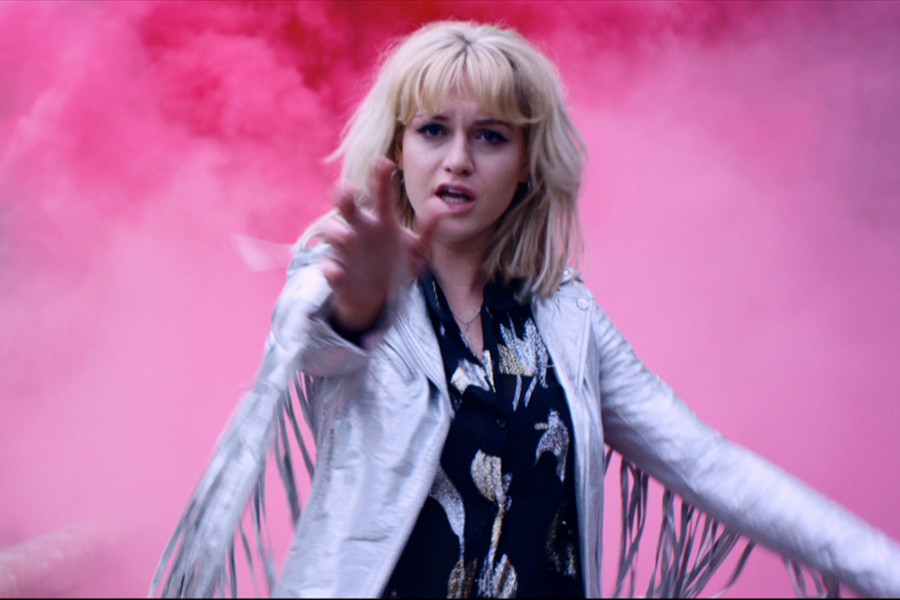 En esta cautivadora imagen del videoclip You, Kerri Watt se acerca directamente a la cámara, irradiando energía y poder. Luce una llamativa chaqueta de cuero plateada brillante que refleja la luz y le añade un toque de estilo audaz.