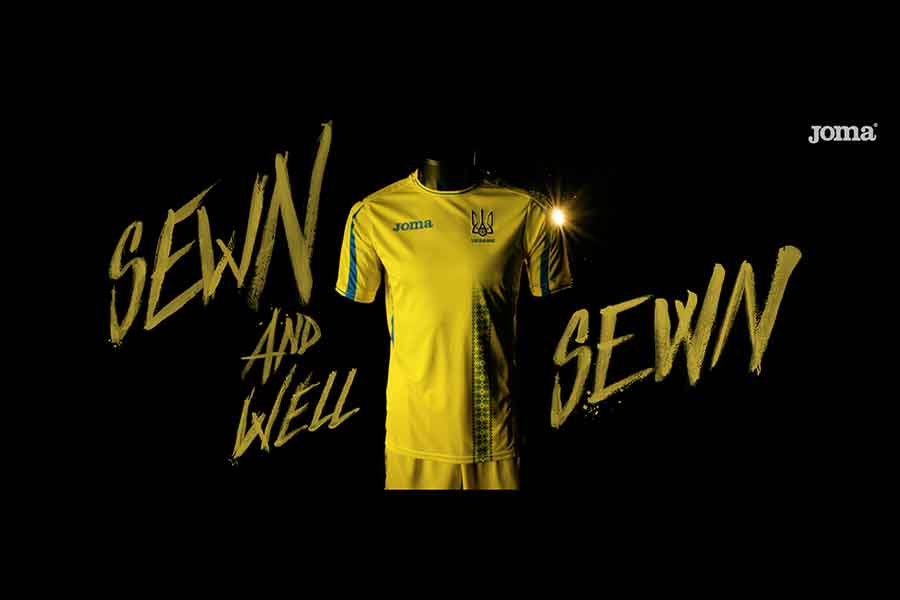 Fotograma del vídeo publicitario de la nueva camiseta de fútbol de la Federación de Fútbol de Ucrania de Joma. En un fondo negro, la camiseta de color amarillo vibrante y detalles en azulina se destaca iluminada. En el centro de la camiseta, la bandera de Ucrania. Un texto en inglés, "Sewn and well Sewn", en letras mayúsculas y trazos pintados a mano en el mismo color amarillo. En el hombro izquierdo de la camiseta, se percibe un destello de luz. En la esquina superior izquierda, el logo de Joma.