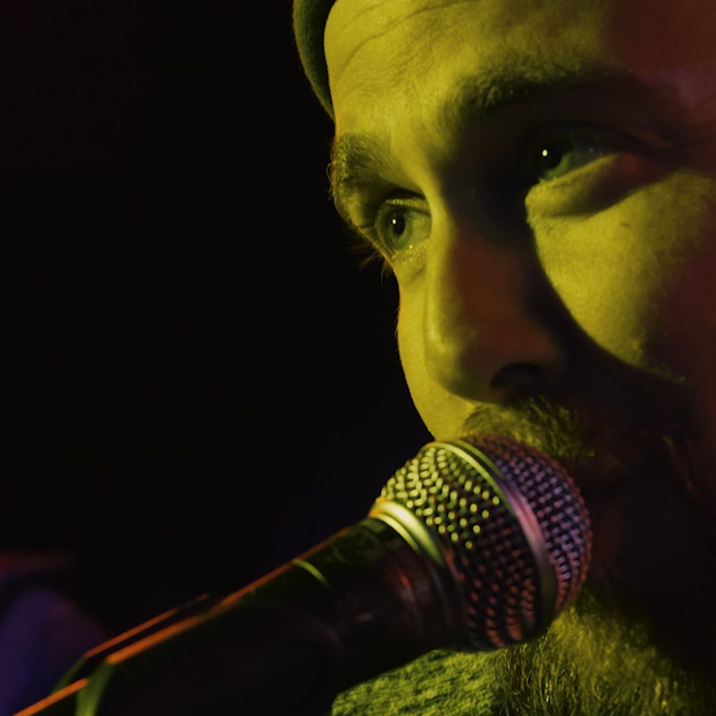 Videoclip Malabarista del Café de Mario Díaz: Primer plano de Mario Díaz con iluminación amarilla en el escenario.