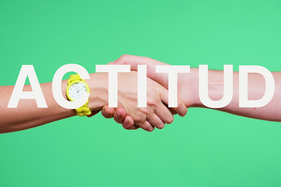 Imagen de un apretón de manos con una mujer usando un reloj amarillo. Palabra "actitud" superpuesta. Video corporativo innovador y divertido creado por Colirio Films para Avance Comunicación. Expertos en branded content y vídeos de producto en España.