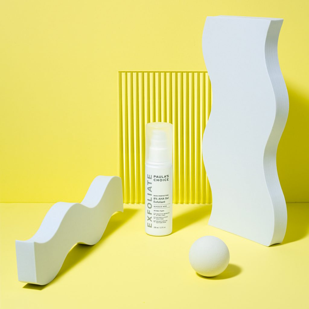 Bodegón de producto cosmético de la marca Paula's Choice en un fondo amarillo. El exfoliante blanco está enmarcado por objetos de diseño blanco en una composición geométrica. Creación de contenido visual innovador por Colirio Films.