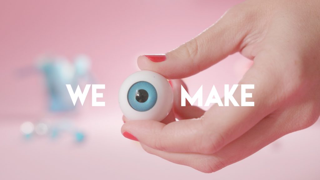 Imagen: Primer plano de una mano sosteniendo un globo ocular con las palabras 'we' y 'make' junto a él, sobre un fondo rosa en el vídeo promocional interno de Colirio Films, productora audiovisual Madrid